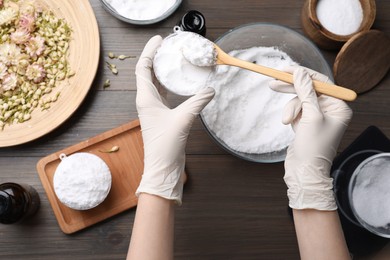 Woman in gloves making bath bomb at wooden table, top view