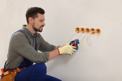 Photo of Electrician in uniform with pliers repairing power socket indoors