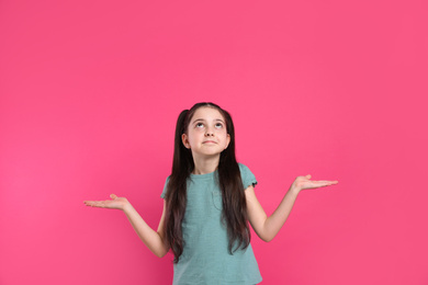 Photo of Portrait of confused little girl on pink background. Thinking about answer for question