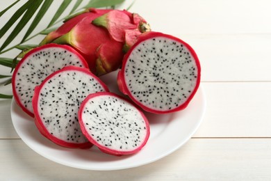 Plate with delicious cut and whole pitahaya fruits on white wooden table