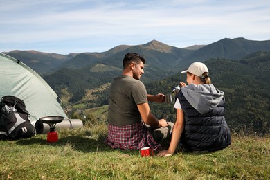 Photo of Couple with coffee enjoying mountain landscape near camping tent, back view