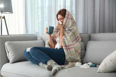 Sick woman wrapped in plaid with cup of hot drink at home. Influenza virus