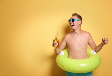 Shirtless man with inflatable ring and bottle of drink on color background