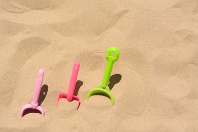 Photo of Bright plastic shovels in sand, space for text. Beach toys
