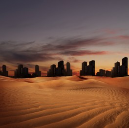 Sandy desert and silhouette of city on horizon in dusk