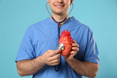 Photo of Doctor with stethoscope and model of heart on light blue background, closeup. Cardiology concept