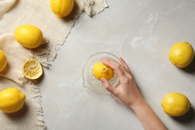 Young woman squeezing lemon with juicer on light table