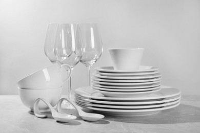 Photo of Set of clean dishware and glasses on grey table against light background