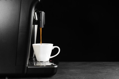 Modern espresso machine pouring coffee into cup on grey table against black background. Space for text