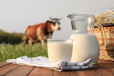 Photo of Milk with hay on wooden table and cow grazing in meadow