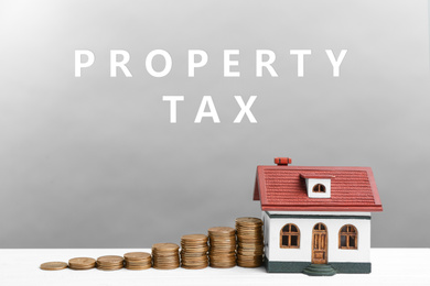Text Property Tax near stacked coins and house model on grey background