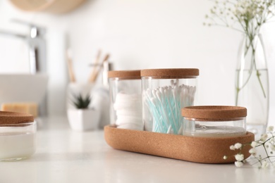Glass jars with cotton pads and buds on countertop in bathroom. Space for text