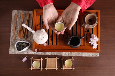 Woman with cup of freshly brewed tea during traditional ceremony at wooden table, top view