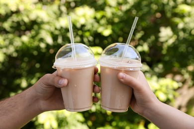 Man and woman toasting with plastic takeaway cups of delicious iced coffee outdoors, closeup