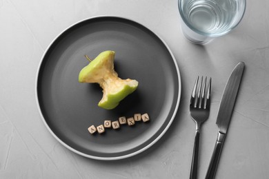 Cutlery, glass near plate with apple core and word Anorexia made of cubes on light table, flat lay