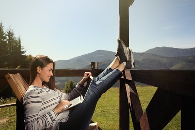 Photo of Young woman working with laptop on outdoor wooden terrace in mountains