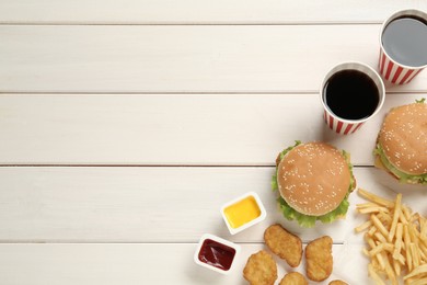Flat lay composition with delicious fast food menu on white wooden table. Space for text
