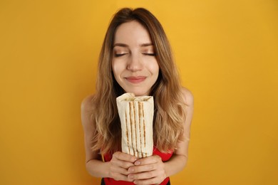Photo of Young woman with delicious shawarma on yellow background