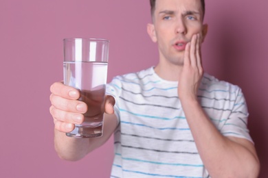 Young man with sensitive teeth and glass of cold water on color background