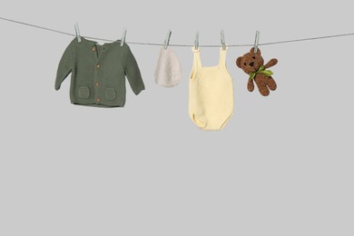 Different baby clothes and toy drying on laundry line against light background