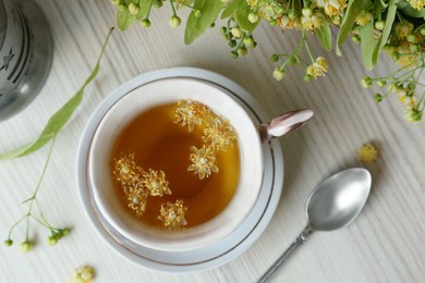 Photo of Cup of aromatic tea with linden blossoms on white wooden table, flat lay