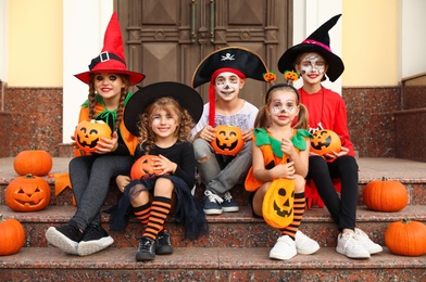 Cute little kids with pumpkins wearing Halloween costumes on stairs outdoors