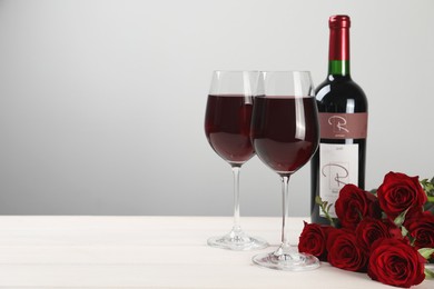 Photo of Bottle and glasses of red wine near beautiful roses on white wooden table. Space for text