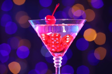 Cocktail with casino dice in glass against blurred lights, closeup