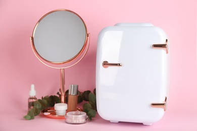 Cosmetic refrigerator and skin care products on pink background