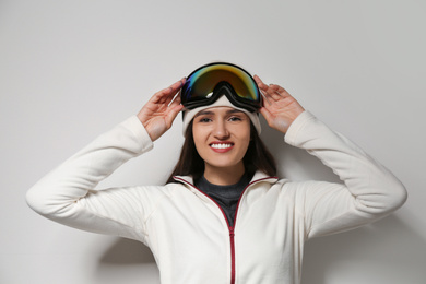 Woman wearing fleece jacket and goggles on light grey background. Winter sport clothes