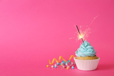 Birthday cupcake with burning sparkler and streamers on pink background. Space for text