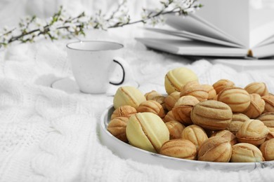 Photo of Delicious walnut shaped cookies with filling, notebook and cup of coffee on white knitted blanket, closeup and space for text. Homemade popular biscuits from childhood