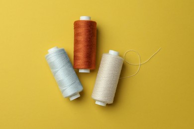 Different colorful sewing threads on yellow background, flat lay