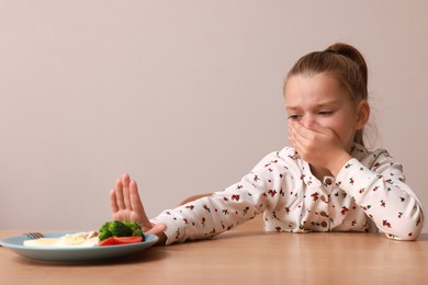 Cute little girl covering mouth and refusing to eat her dinner at table on grey background
