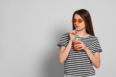 Beautiful young woman drinking juice from plastic cup on light grey background. Space for text