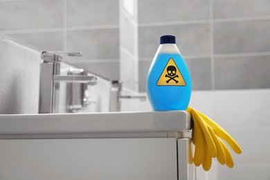 Bottle of toxic household chemical with warning sign and gloves in bathroom, space for text