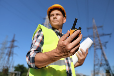 Professional electrician near high voltage tower, focus on hand with portable radio station