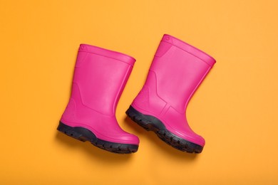 Pair of bright pink rubber boots on orange background, top view