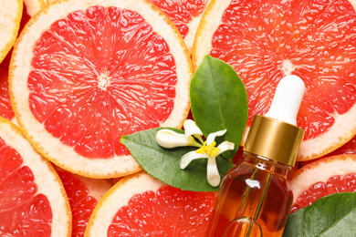 Bottle of citrus essential oil and flower on pile of grapefruit slices, flat lay. Space for text