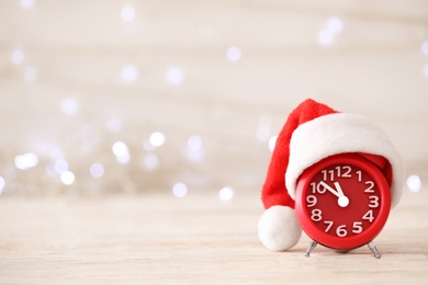 Alarm clock with decor on white wooden table against blurred Christmas lights. New Year countdown