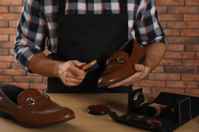 Craftsman taking professional care of brown leather shoes in workshop, closeup