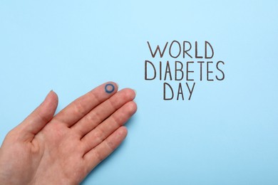 Photo of Woman showing finger with drawn blue circle near text World Diabetes Day on color background, closeup