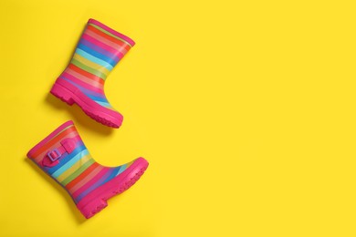 Striped rubber boots on yellow background, top view. Space for text