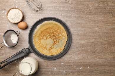 Frying pan with delicious crepe and ingredients on wooden table, flat lay. Space for text
