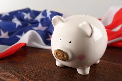 Piggy bank and American flag on wooden table, closeup