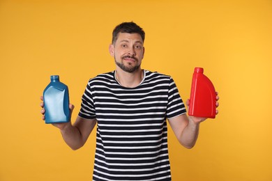 Confused man holding two containers of motor oil on orange background