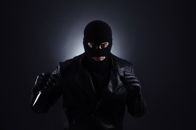 Photo of Man wearing knitted balaclava with knife on black background
