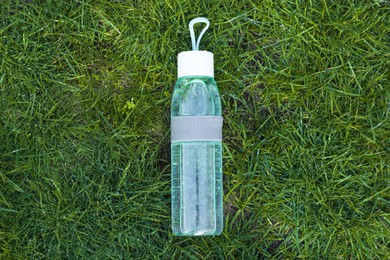 Photo of Glass bottle of fresh water on green grass outdoors, top view