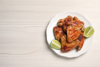 Photo of Plate with delicious fried chicken wings and lime on white wooden table, top view. Space for text