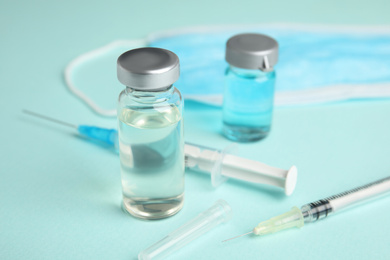 Vials, syringes and surgical mask on turquoise  background. Vaccination and immunization